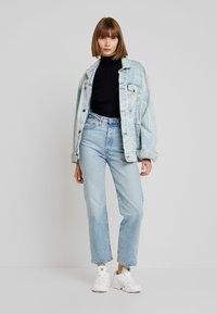 Lichtblauwe denimjas gelaagd over een zwarte coltrui, gecombineerd met lichtblauwe jeans en witte sneakers; comfortabele pasvorm en klassiek ontwerp.
