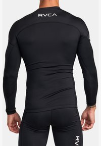 Zwarte rashguard met lange mouwen, gemaakt van rekbaar materiaal, heeft een gestroomlijnde pasvorm en het RVCA-logo op de achterkant. Soepele textuur.
