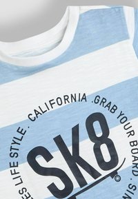 Světle modré a bílé pruhované tričko s kulatým výstřihem a černým tištěným textem "SK8" a "CALIFORNIA. VZÍT SVOU PRKNO."