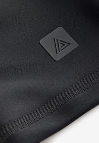 Schwarzer Stoff mit glatter Textur zeigt ein kleines schwarzes quadratisches Abzeichen mit einem ausgeschnittenen dreieckigen Logo. Nahtstiche sind entlang des Randes sichtbar.