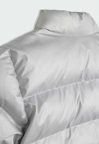 Srebrna puffer jakna s visokim ovratnikom. Ima glatku, sjajnu teksturu i ušivene horizontalne panele za izolaciju.