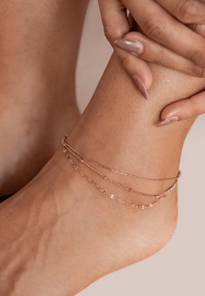 Rose gold ankle bracelet features three chains of varying lengths, showcasing a delicate design with textured and polished links against skin.