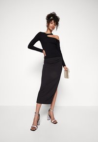 Zwarte één-schoudertop met een uitsnede, gecombineerd met een strakke zwarte midi-rok met een zijsplit. Accessoires zijn sprankelende block-heels sandaal.