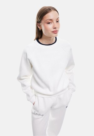 Vit sweatshirt med marinblå ribbad halsringning, raglanärmar och avslappnad passform. Kombinerad med vita sweatpants med broderad text.