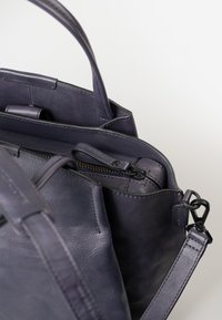 Borsa a tracolla in pelle di un viola scuro con due manici, una tasca interna con zip e una tracolla rimovibile con hardware nero.