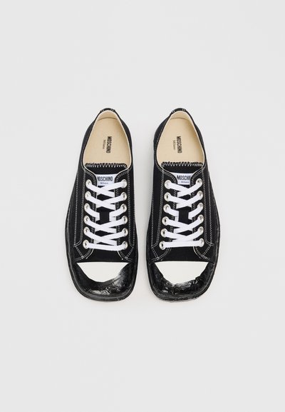 Pair of black canvas sneakers with white laces and toe caps, slightly worn and creased, branded Moschino Milano inside.