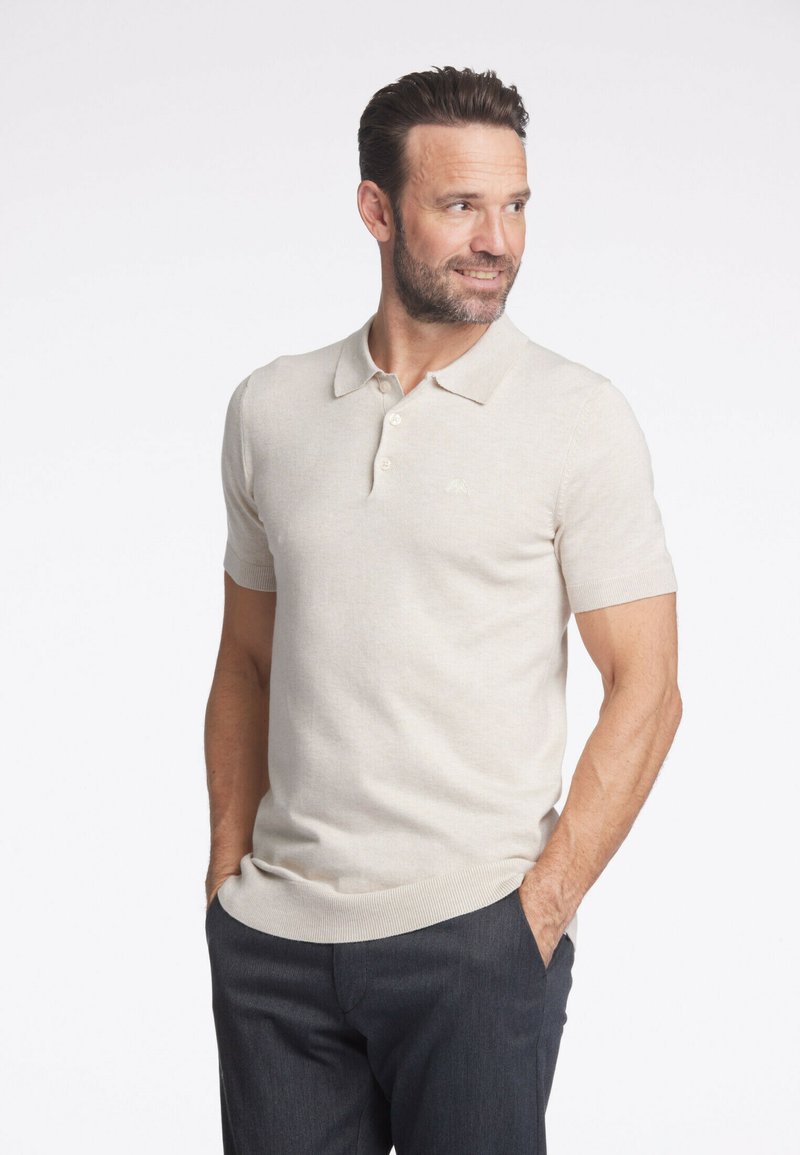 Beige kortärmad polo skjorta i mjukt stickat tyg, med klassisk krage och treknappslå, samt diskret logotypdetalj på bröstet.