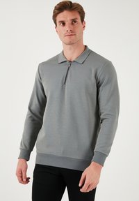 Sivý dlhý rukáv polo sveter v textúrovanej látke s polovičným zipsom na golieri. Obsahuje rebrované manžety a lem. Jednoduchý, minimalistický dizajn.