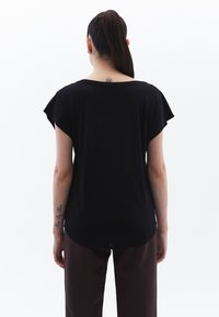 Musta lyhythihainen paita löysällä istuvuudella, pyöreällä kaula-aukolla ja kaartuvalla helmalla. Sujuva pinta, monipuolinen arkikäyttöön.