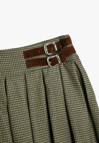 Groen geruit rokje met plooien, voorzien van twee bruine suède bandjes met zilveren gespen bij de taille voor het vastmaken. Textuur van de stof is duidelijk zichtbaar.