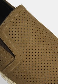 Bruine geperforeerde leren instapper met een gestructureerd oppervlak en elastische zijpanelen. Bevat een lichtgekleurde zool en een afgeronde neusontwerp.