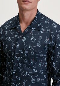 Marineblauwe short-sleeve shirt met een patroon van ski-motieven, gondels en Zwitserse bezienswaardigheden in wit en rood. Met button-down kraag en borstzak.