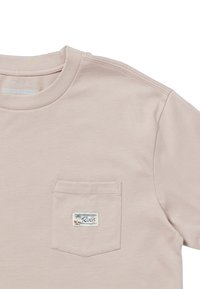 Camiseta de algodón rosa claro con escote redondo y un bolsillo en el pecho izquierdo que presenta una etiqueta con un diseño de palmera. Textura suave y de peso medio.