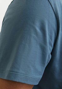 Camisa de manga corta en una tela azul suave. Textura blanda con cuello redondo y un detalle de costura visible en el dobladillo.
