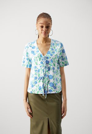Short-sleeve, floral blouse in white fabric with blue and green flower patterns. Features a V-neckline and tie detail at the front.