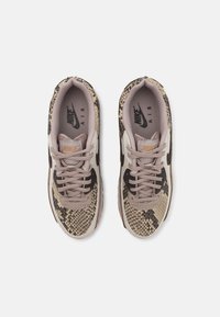 Teniske s teksturiranim uzorkom zmijske kože u nijansama bež i smeđe; imaju svetloružičaste vezice i crni logo Nike s bočne strane.