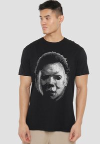 Black cotton t-shirt featuring a graphic print of a mask in white and gray, with detailed facial features and dark hair accents.