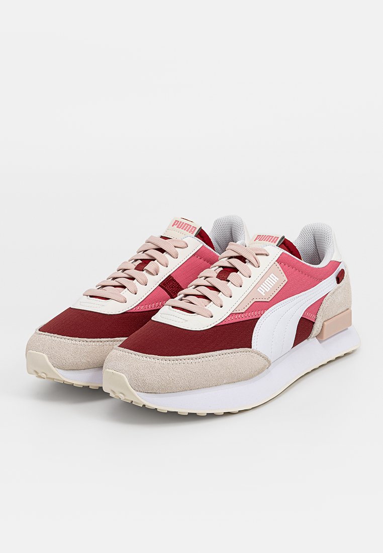 Une paire de baskets Puma en bordeaux, rose, beige et blanc avec des lacets et des semelles blanches rembourrées sur un fond uni.
