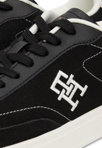 Mustat mokkanahkan tennarit, joissa valkoinen logo, kontrastivalkoinen ompelu ja mustat nauhat. Niissä on sileä nahkainen kieli ja teksturoitu päällinen.