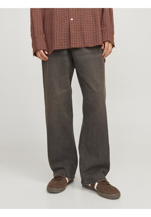 Person wearing loose-fitting faded black jeans, brown checkered shirt, and brown sneakers standing on a light gray floor.