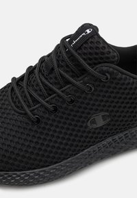 Černá síťovaná teniska s texturovanou podešví, kulatými černými tkaničkami, polstrovaným límcem a logem na boku.