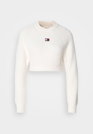 Kaprisk hvit genser med ribbestruktur, lange ermer og rund hals. Har et lite, merket logo på brystet.