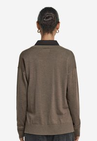 Brun tröja med svart krage, mjuk textur och avslappnad passform. Har långa ärmar och ribbade muddard, perfekt för lager-på-lager.