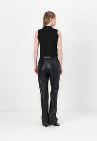 Black cropped sleeveless top paired with high-waisted black leather pants. Smooth texture and fitted design, accentuating the silhouette.