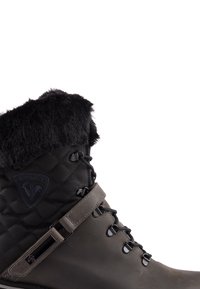 Stivale invernale trapuntato nero con collare in pelliccia sintetica, parte inferiore in gomma, design con lacci e un patch con logo sul lato.