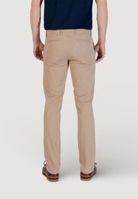 Pantalones beige con un diseño de pierna recta, hechos de una tela suave. Cuentan con dos bolsillos traseros y se combinan con zapatos oscuros.