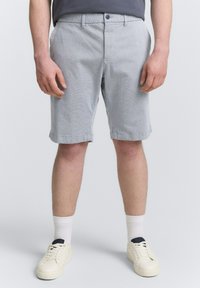 Hellgraue Shorts mit strukturiertem Muster, seitlichen Taschen und umgeschlagenen Säumen. Kombiniert mit weißen Socken und cremefarbenen Sneakers.