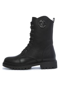 Botte de combat noire en cuir avec lacets, semelle épaisse et emblème métallique de marque près du haut, côté extérieur.