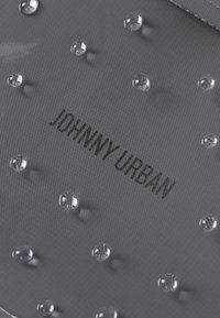 Tejido gris con texturas circulares en relieve y gotas de agua claras. Logotipo "JOHNNY URBAN" impreso en texto negro.