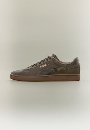 Baskets basses marron Puma avec lacets à l’avant, bande latérale texturée et semelle ainsi que logos latéraux siglés sur fond uni.
