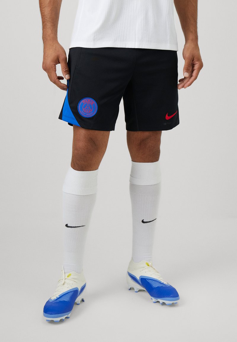 Sorte shorts med blå sidelæbe og rød Nike-logo, båret med hvide sokker og blå fodboldstøvler med struktureret design.