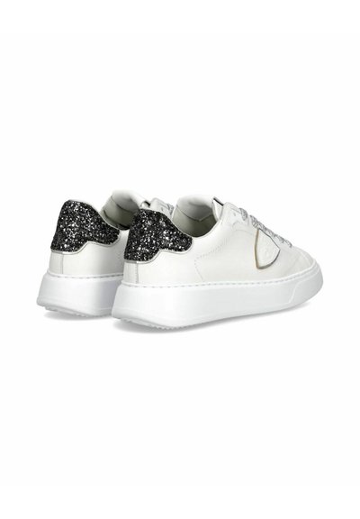 Witte lage sneakers met dikke zolen, zwarte glinsterende hielaccenten en zilveren glinsterende veters, gezien vanaf de achterkant en zijkant.