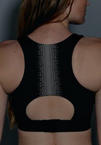 Svart sportbh med skuren rygg, texturerad tyg och en central remsa av små reflekterande prickar för synlighet.