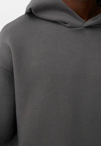 Felpa con cappuccio grigio scuro realizzata in un tessuto morbido, caratterizzata da una vestibilità rilassata e un design semplice senza motivi o dettagli visibili.