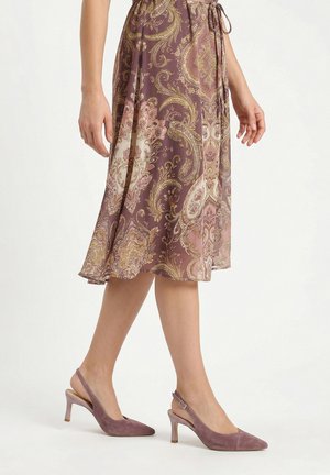 Frau trägt einen violetten Paisley-Midirock und mauvefarbene Wildleder Slingback-Schuhe mit spitzen Zehen und niedrigen Absätzen.