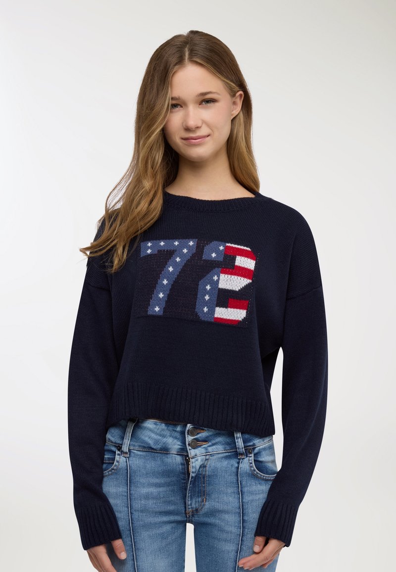 Maglione blu navy con maniche lunghe e orlo a coste, presenta un grande motivo lavorato a maglia "72" in rosso, bianco e blu con motivi a stelle.