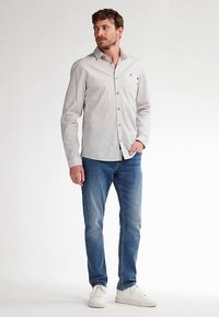 Herenoverhemd met knopen, voorzien van verticale witte en marineblauwe strepen, lange mouwen en een borstzak. Gecombineerd met een blauwe spijkerbroek en witte schoenen.