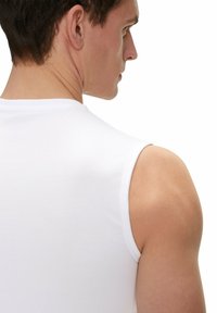 White sleeveless shirt made of smooth cotton, fitted design hugging the torso, minimal stitching, with a rounded neckline showcasing the shoulder.