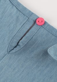 Hellblaue Denim-Stoff mit einer schmalen Öffnung und einem rosa Knopfdetail. Die Nähte sind entlang der Kanten sichtbar.