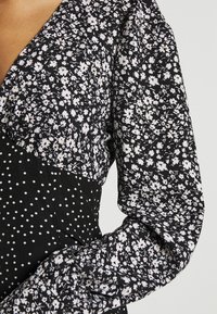Vestido negro con estampados florales y de lunares, que presenta un escote en V y mangas largas con fruncidos. Fabricado en tejido ligero.