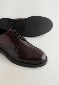 Braune Leder-Dressschuhe mit glatter Oberfläche, Schnürdesign und schwarzer Gummisohle. Eigenschaften umfassen dezente Nähte und eine abgerundete Zehenpartie.