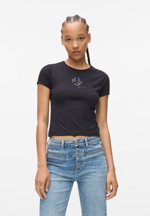 Zwarte cropped t-shirt met korte mouwen, voorzien van een zilverkleurig logo op de borst. Gemaakt met hoge taille lichtblauwe denim jeans met een knopenrij.