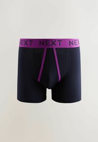 Boxer-briefs navy avec une large ceinture élastique violette ornée du texte répétitif "NEXT" et un design de poche avant fonctionnelle.