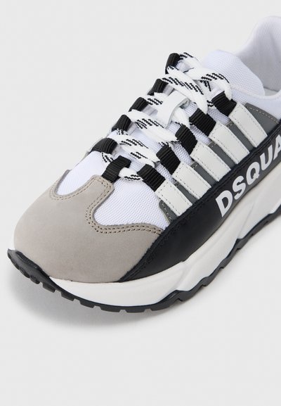 Chaussure de sport avec un mélange de mesh blanc, de daim gris et de cuir noir. Caractérisée par des lacets rayés noirs et blancs et le logo "DSQUAR" bien en évidence.