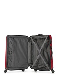 Maleta rígida roja con un zipper abierto, que cuenta con un interior gris, un bolsillo de malla y correas cruzadas para asegurar los objetos. Cuatro ruedas para movilidad.