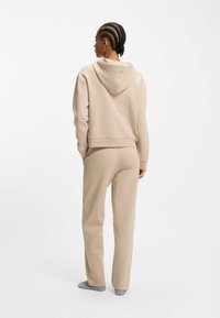 Sudadera corta beige con cordón y pantalones deportivos beige a juego. Fabricada con tela suave, con textura lisa y ajuste relajado.